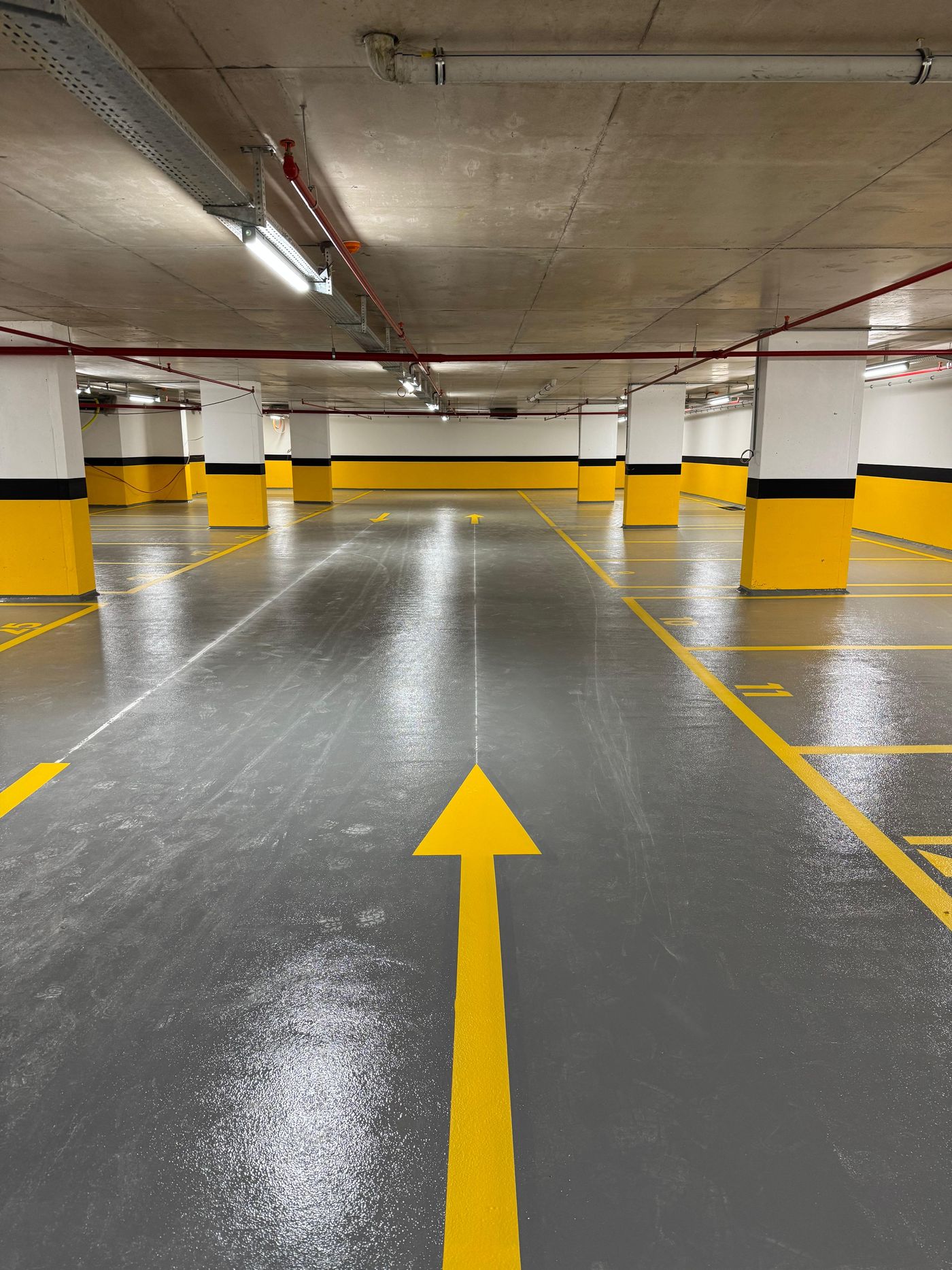 Gri epoksi zeminli kapalı otoparkta sarı yön oku, sarı-siyah kolon boyası ve numaralı park yerleri