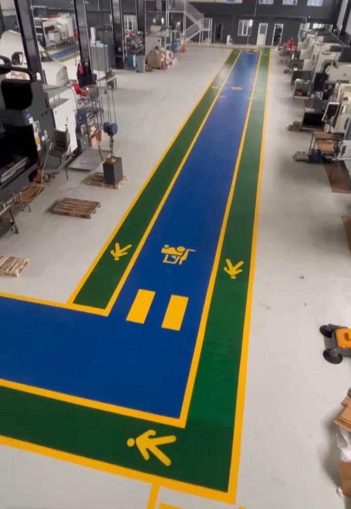 Fabrika içinde mavi kenarlı yeşil yürüyüş yolu ve piktogramlar