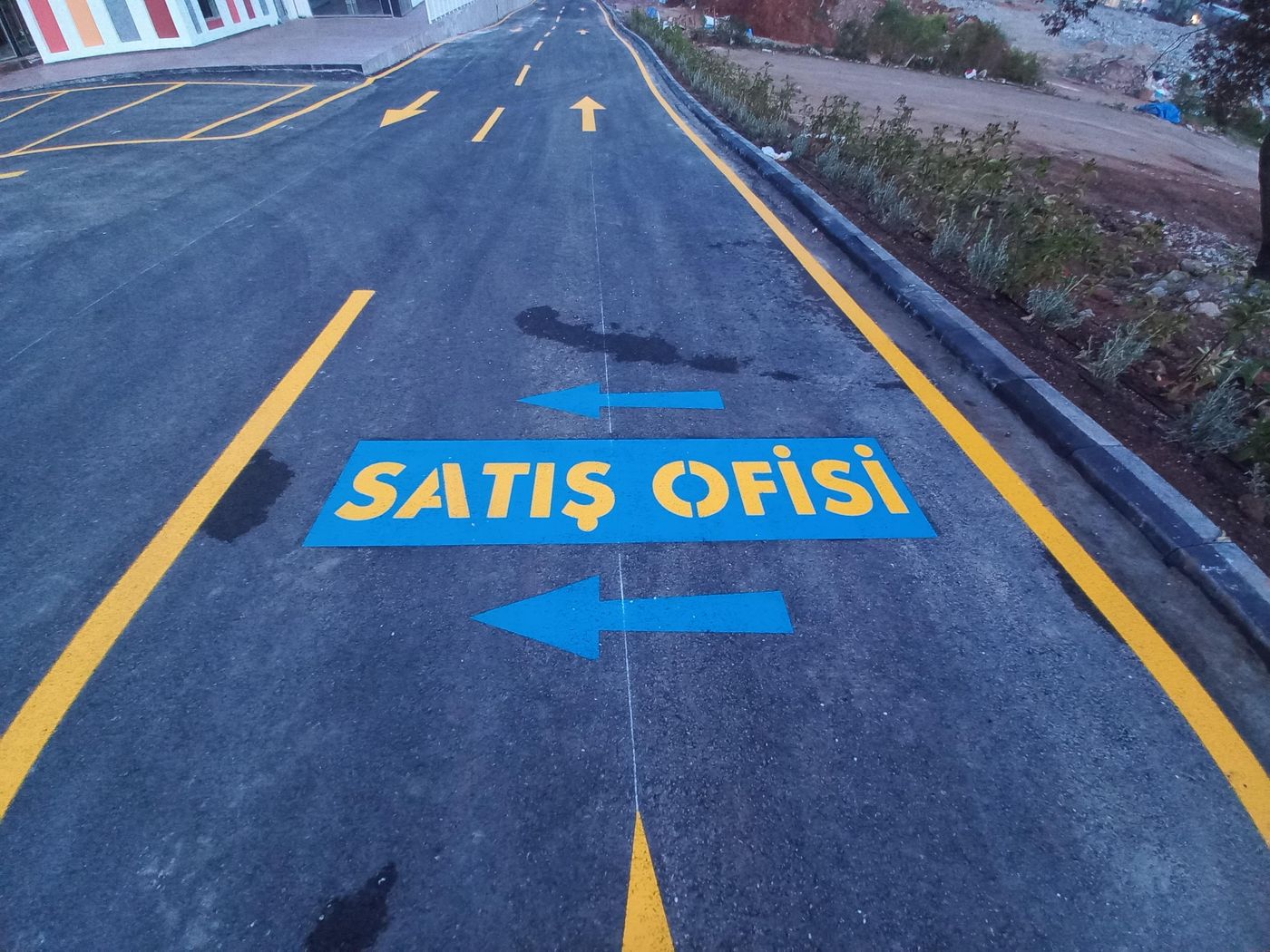 Asfalt yol üzerinde sarı şerit çizgileri, mavi Satış Ofisi yönlendirme yazısı ve oklar